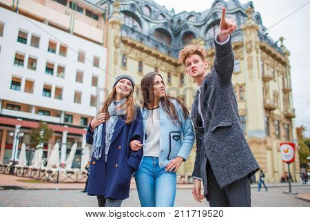 A young man in a coat on the street points out the hand of the beautiful girls. Autumn city, tourist.