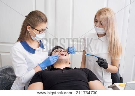 Two Female Dentists Checking Up Patient Teeth With Dental Tools - Mirror And Probe At Dental Clinic