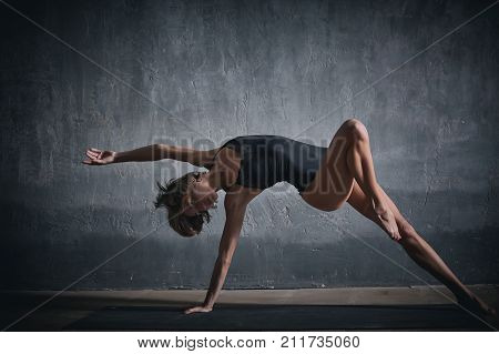 Beautiful sporty fit yogini woman practices yoga asana Wild Thing Pose in the dark hall.
