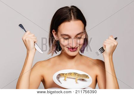 Young brunette girl looks at a lizard in a plate and is going to eat it
