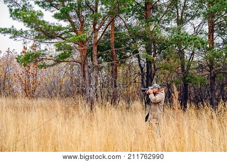 Photographer in a raincoat pictures of nature on the background of pine trees
