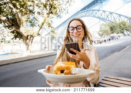 Young woman enjoying traditional portuguese meat sandwich called Francesinha, sitting at the bar with famous bridge on the background in Porto city, Portugal