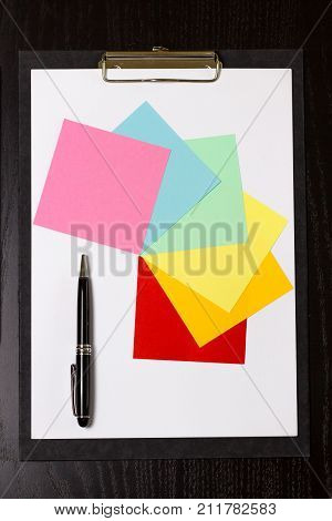 Clipboard with white paper pen and colored notes on black wooden table
