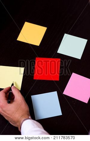 Hand with pen pointing on colored notes black background