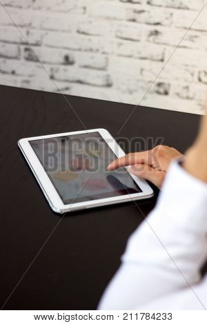Person pointing with hand on tablet. Tablet on black wooden table