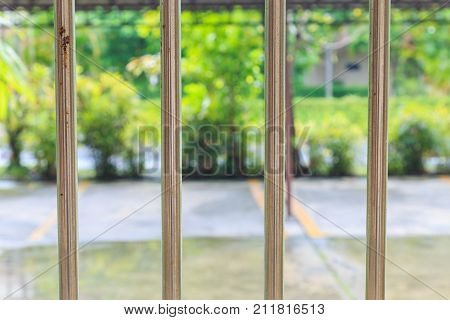 An old stainless rail fence and outside is parking and garden at raining day.