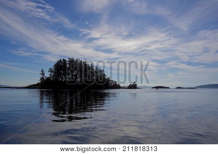 A Small Tree Covered Island In The Gulf Islands Of Southern Bc Is Reflected In The Calm Blue Waters 