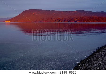 One of BC Ferries' boats passes by Mount Tuam on Salt Spring Island lit by the bright red dawn light which also gives a warm cast to the mountainside while the beach on Portland Island remains in shadow.