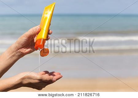 Woman hands putting sunscreen from a suncream bottle on the beach