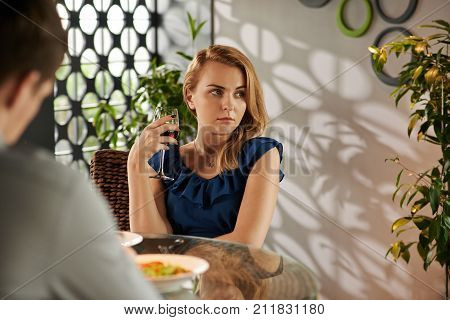 Unhappy pretty young woman drinking wine during blind date in restaurant