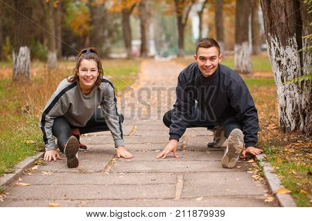 A couple in love doing sports in the park in the fall. Stretch the muscles of the legs and sit down.