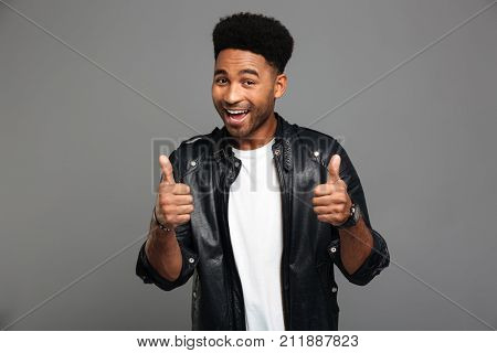 Close-up portrait of african slylish man showing thumbs up gesture with two hands, looking at camera, isolated on gray background