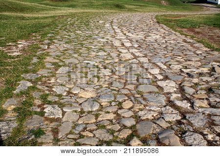 Ancient winding road paved with cobblestone and overgrown by grass.