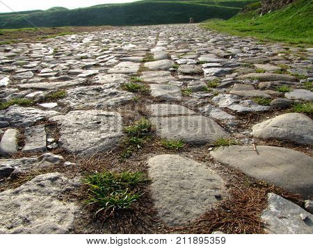 Ancient road paved with cobblestone overgrown by grass and going up through hills. Perspective view. Bottom view.