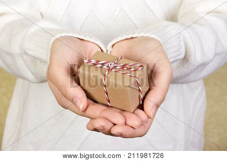 Portrait of attractive cheerful girl in sleeveless sports white shirt holding gift box with red bow over canvas background.