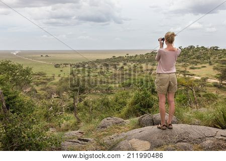 Female tourist looking through binoculars on African safari in Serengeti national park, Tanzania, Afrika.