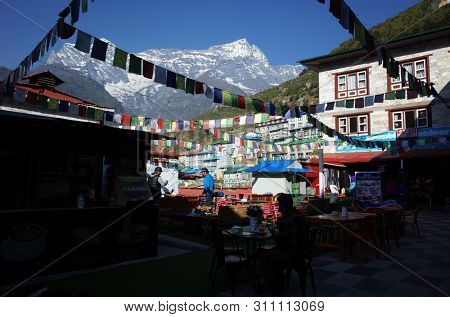 Namche Bazaar, Nepal - May 11, 2019: Outdoor cafe in town centre decorated with praying flags, view over Kongde mountain in early morning, Sagarmatha national park, Khumbu valley, Himalayas