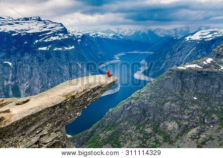 Norway, A woman sits on the mountain's cliff edge of Trolltunga throning over Ringedalsvatnet watching the  the snowy Norwegian mountains near Odda, Rogaland, Norway.
