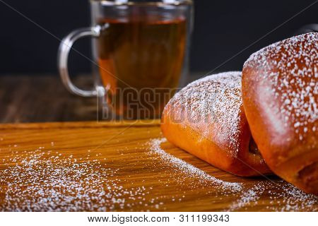 Two Buns Dusted With Icing Sugar And A Cup Of Black Tea On The Background. Top View