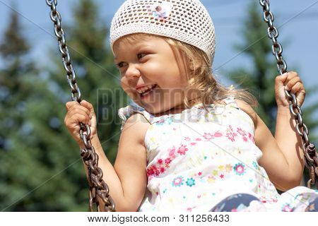 Smiling Happy Little Girl Swinging In Summer Park
