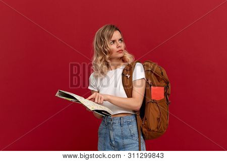 Confused Blond Girl With Curly Hair In A White T-shirt Trying To Find Itinerary With The Map Holding