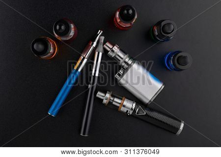 Electronic Cigarettes Or Vaping Devices And Bottles With Vape Liquid On Dark Background