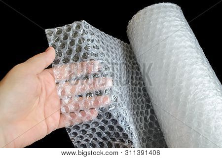 Woman Hand Holdind A White Transparent Bubble Wrap On A Black  Background. Material For Packing Frag