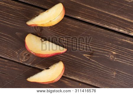 Group Of Three Slices Of Fresh Dark Red Pear Anjou Flatlay On Brown Wood