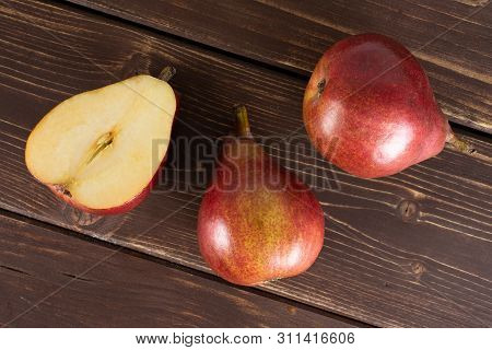 Group Of Two Whole One Half Of Fresh Dark Red Pear Anjou Flatlay On Brown Wood