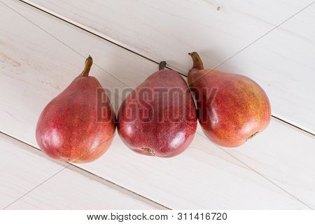 Group Of Three Whole Glossy Fresh Dark Red Pear Anjou Flatlay On White Wood