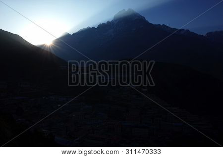 First view of morning sun from behind Thamserku mountain, Namche Bazaar village in shade, Sagarmatha national park, Khumbu valley, Himalayas, Nepal
