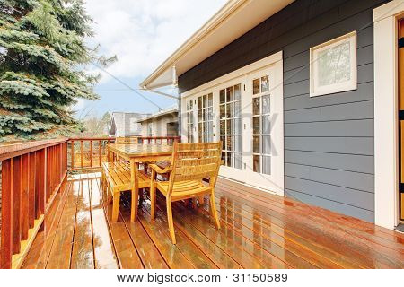 Houten dek met meubels en grijs huis.