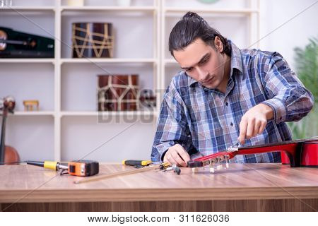 Young handsome repairman repairing guitar