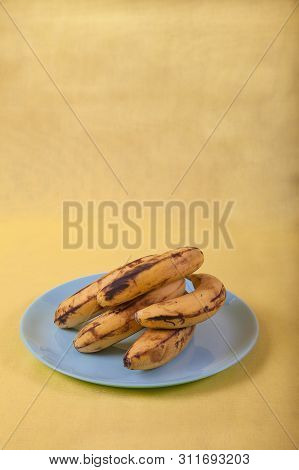Ugly Bananas Lie On A Blue Plate On A Yellow Background . Copy Spaes