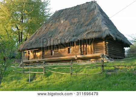 Wooden House With A Thatched Roof Surrounded By Greenery.