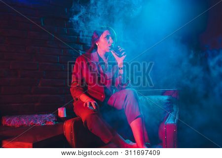 Woman Smokes A E-cigarette Lying On The Bed In The Room. Smokers Concept Vaping.