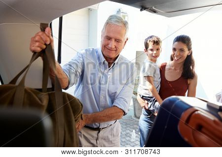 Senior white man packing car boot with holiday luggage, watched by his adult daughter and grandson