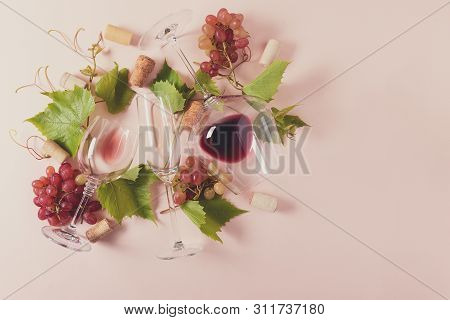 Assorted Wineglasses With Red, Rose And White Wine, Grape, Leaves And Cork Lying On Pink Background.