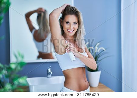 Beautiful brunette woman using deodorant in the bathroom