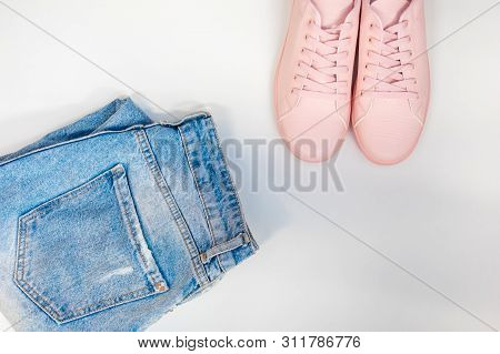 Flat Composition With A Set Of Clothes, Jeans And Pink Sneakers. Top View On A White Background.