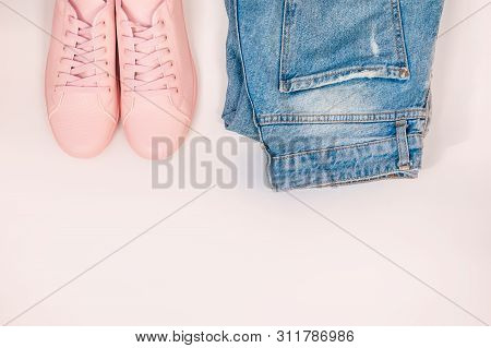 Flat Composition With A Set Of Clothes, Jeans And Pink Sneakers. Top View On A White Background.