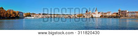 Autumn Panorama Of Charles Bridge And Historic Buildings On The Riverside In Prague Captured From St