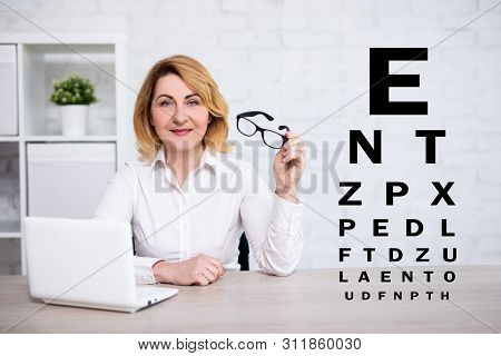 Eyevision Test Chart And Mature Business Woman Using Laptop And Holding Eyeglasses In Modern Office 