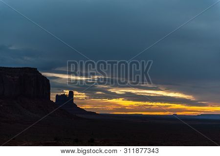 Early Morning Light Of Dawn, Contasted Against The Black Mesa Walls Of Monument Valley.