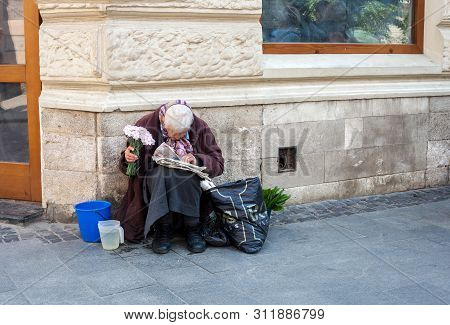 Lviv, Ukraine - 26 May 2019: Elderly Woman Selling Flowers. Old Woman Sitting On Street And Reading 