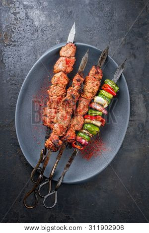 Traditional Russian shashlik on a barbecue skewer with vegetable and onion as top view on a modern design cast iron plate with copy space 