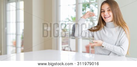 Wide angle picture of beautiful young girl kid wearing casual sweater gesturing with hands showing big and large size sign, measure symbol. Smiling looking at the camera. Measuring concept.