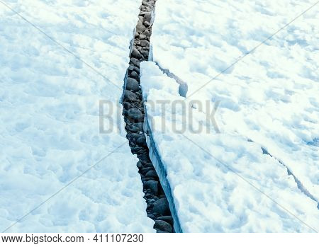 Large Crack In Permafrost Ice Revealing Dry Rocks Hidden Beneath.