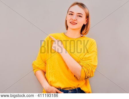 Horizontal Picture Of Young Good-looking Female Isolated On Grey Background, Pointing Leftwards With