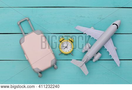 Air Plane, Mini Travel Luggage And Alarm Clock On B;ue Wooden Background. Time To Travel. Top View